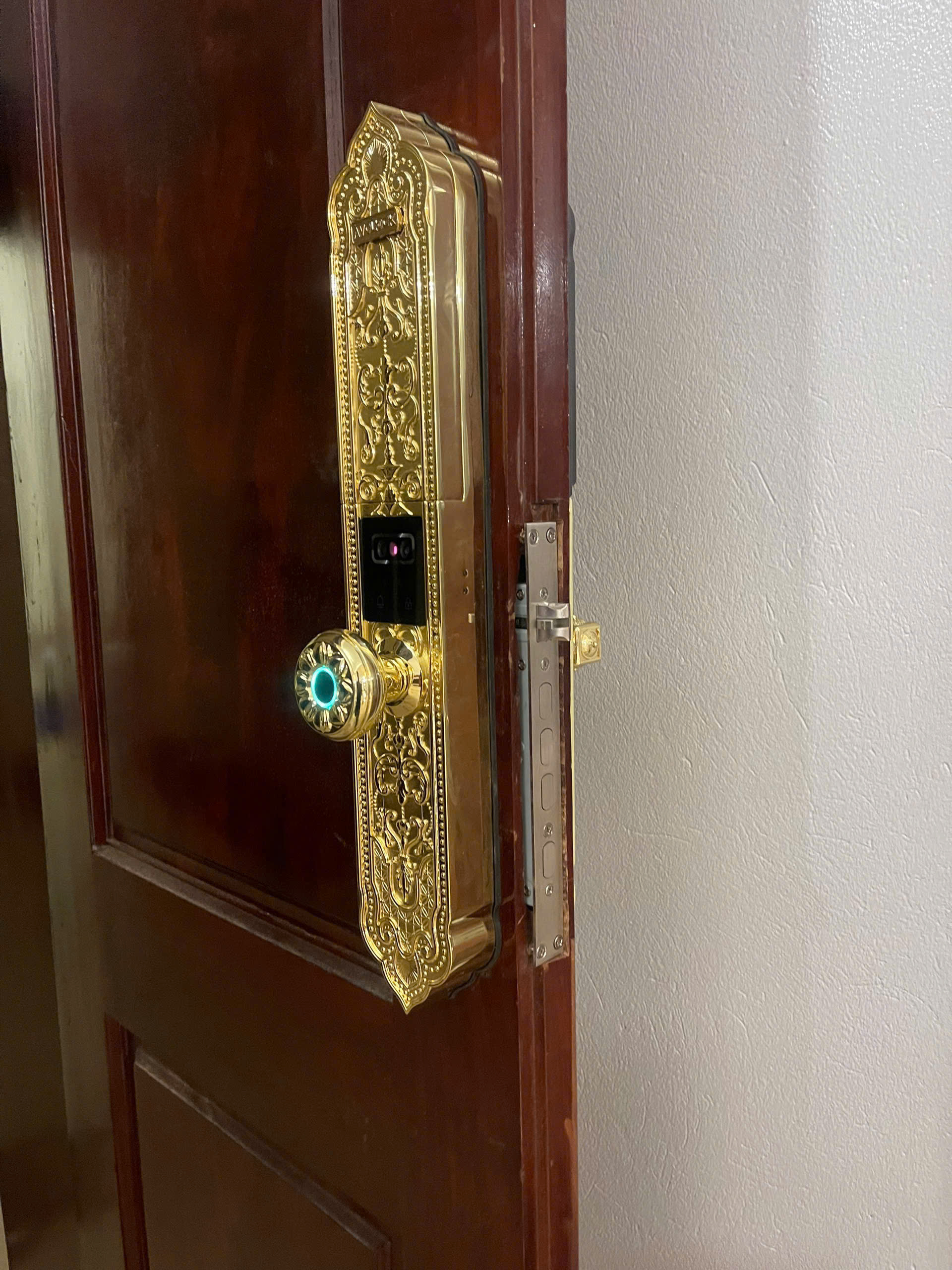 Cận cảnh núm vân tay và mặt khóa Avolock AC-996F từ góc nghiêng, thấy viền cạnh khóa và then khóa trên cạnh cửa gỗ