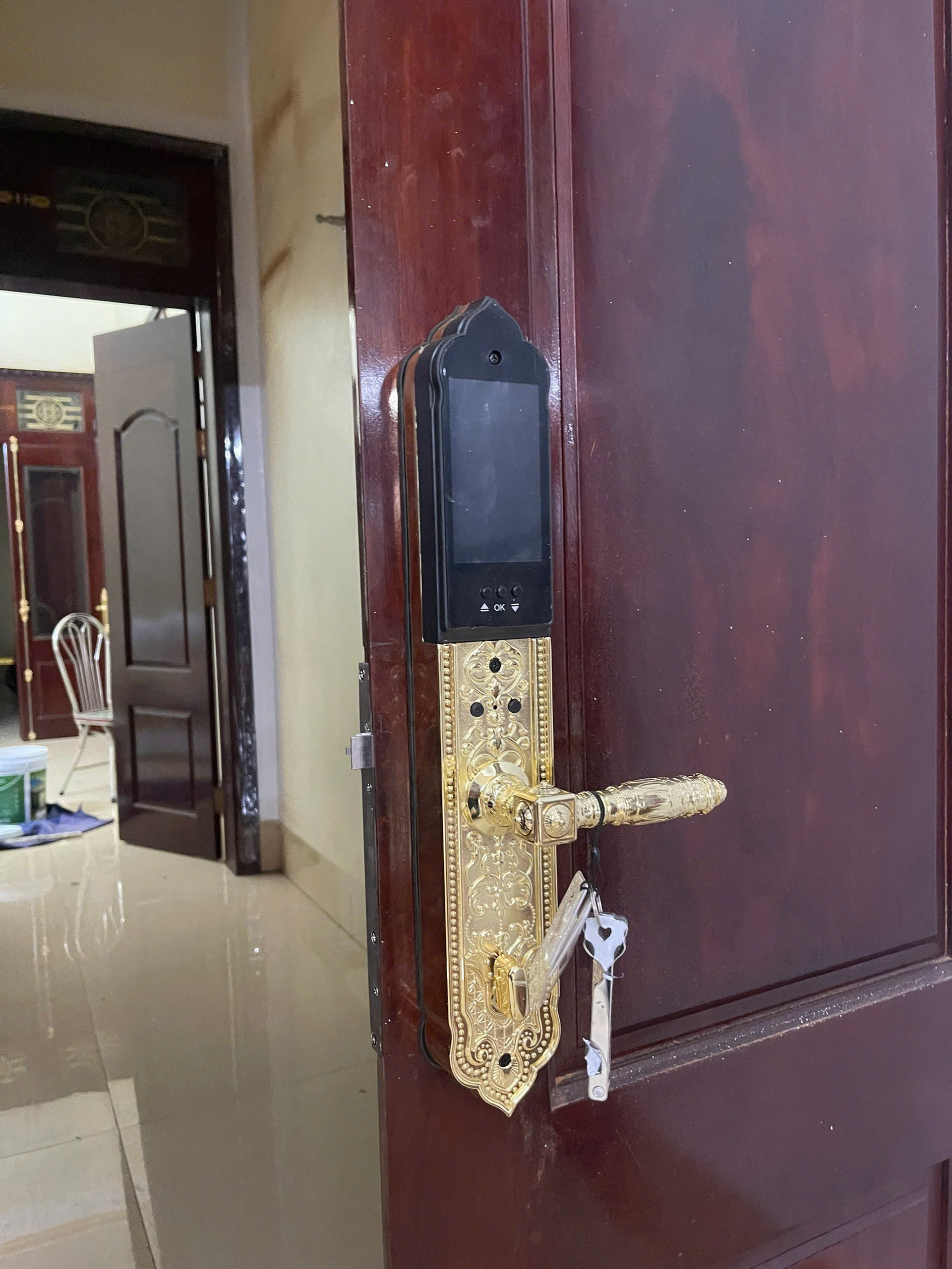 Khóa Avolock AC-996F lắp đặt thực tế trên cửa gỗ nâu đỏ, mặt khóa mạ vàng nổi bật, có chùm chìa cơ